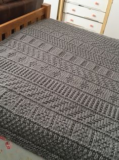 a bed with a gray blanket on top of it next to a brown couch and white drawers