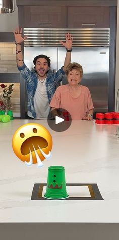 two people standing in front of a kitchen counter with an emoticive face on it