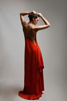 a woman in a red dress is posing with her back to the camera and hands on her head