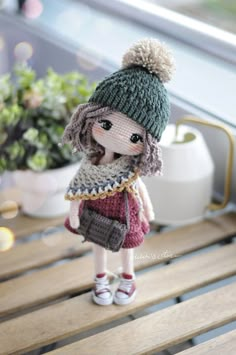 a doll is wearing a knitted hat and dress on a wooden bench next to a potted plant