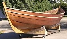 an old wooden boat is on display in front of a tree and sidewalk with no one around it