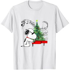 a white t - shirt with a dog playing the piano next to a christmas tree