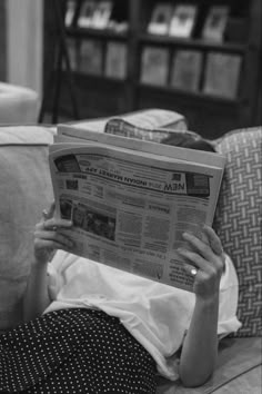 a woman laying on top of a couch reading a newspaper