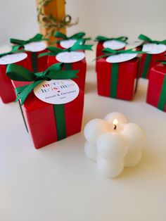 small red gift boxes with green bows and candles in front of them on a table