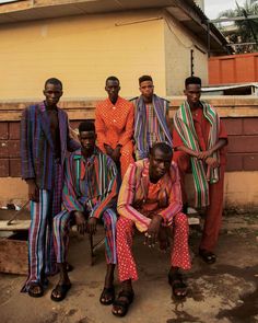 a group of men sitting next to each other in front of a yellow building with red and green stripes