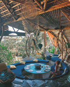 a woman sitting on top of a blue couch in a room filled with lots of plants