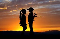 two people are standing in the sunset with their backs to each other and one is holding a flower