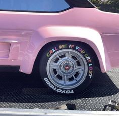 a pink car parked in a parking lot with its wheels painted like the word california