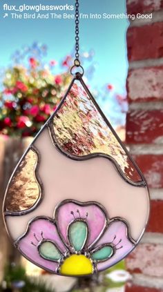 a stained glass sun catcher hanging from a brick wall with flowers in the window behind it