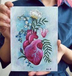 a painting of a heart with flowers and leaves in it's center being held by a woman