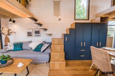 a living room filled with furniture next to a wooden table and stair leading up to a loft