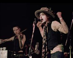 two people on stage singing into microphones with one person wearing a hat and tie