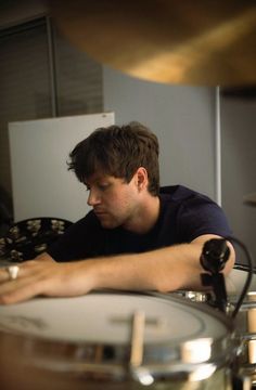 a man sitting behind a drum set with his hands on the drumstick and looking down