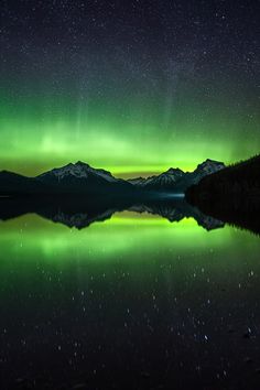 the aurora bore is reflected in water with mountains in the background and stars in the sky