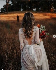 the back of a bride's dress walking through a field with her bouquet in hand