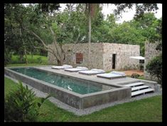 an outdoor swimming pool surrounded by trees and lawn chairs with white cushions on the edge