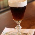 a tall glass filled with liquid sitting on top of a wooden table next to a napkin