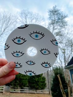 a person holding up a white disc with blue eyes on it in front of a house