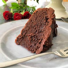 a piece of chocolate cake on a plate with a fork and roses in the background