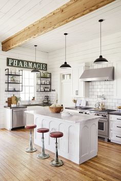 a kitchen with white walls and wooden flooring has an island in the middle that is surrounded by stools