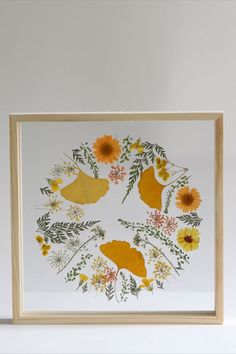 a painting with yellow flowers and leaves on white paper next to a wooden framed object