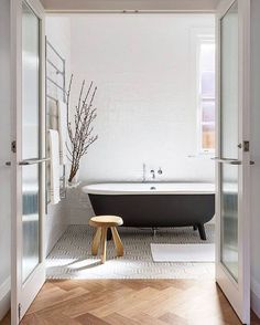 a bath tub sitting next to a wooden stool in a white and black bathroom on top of a tiled floor