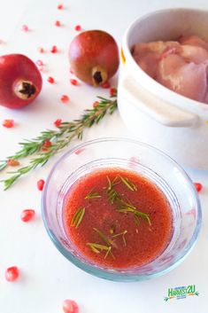 pomegranate in a glass bowl next to fresh fruit and herbs on a white table