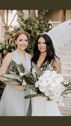 two beautiful women standing next to each other holding flowers and greenery in their hands