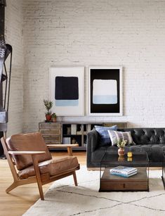 a living room with white brick walls and black leather couches, coffee table, and chairs