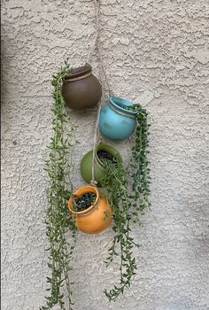 three hanging pots with plants in them on the side of a building, next to a wall