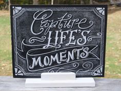 a chalkboard sign that says capture life's moments on the front of a wooden table