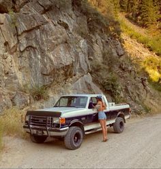 a woman standing in the back of a pick up truck next to a large rock