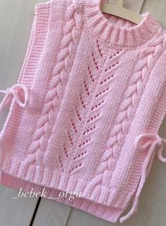 a pink knitted sweater hanging from a hook on a white wooden door with the tag attached to it