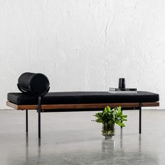 a black bench with a plant on it in front of a white wall and concrete floor