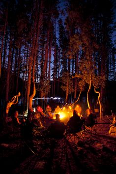 people sitting around a campfire in the woods at night with bright lights on them