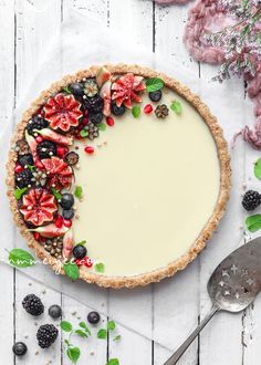 a pie with fruit on top is sitting on a white table next to berries and leaves