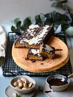 two pieces of chocolate cake on a wooden plate with nuts and sauces around it