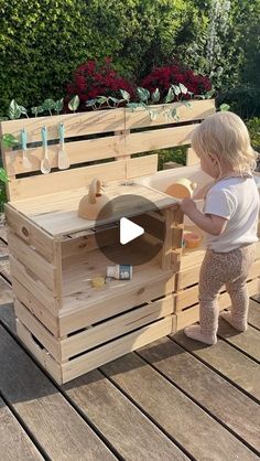 a toddler playing with a wooden toy box on a deck in front of some flowers