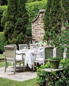 an outdoor table and chairs in the middle of a garden with green plants around it