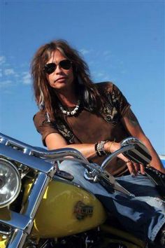 a man sitting on the back of a motorcycle with sunglasses on his head and long hair