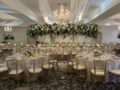 a banquet room set up for a formal function with white flowers and greenery on the ceiling