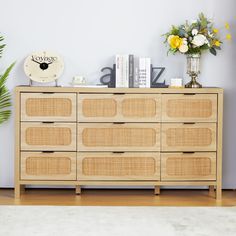 a wooden dresser with flowers and books on it next to a clock, plant and other items