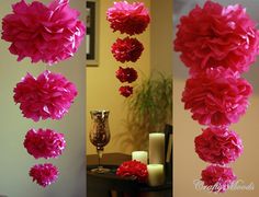 pink tissue flowers hanging from the ceiling in front of a table with candles and vases