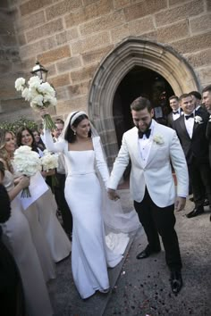 a bride and groom walking out of the church after their wedding ceremony, with guests in the background