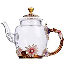 a glass teapot with flowers painted on the side and gold trimming around it