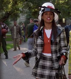 a woman in a plaid coat and hat walking down the street with her arms outstretched