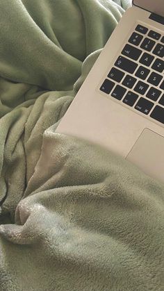 an open laptop computer sitting on top of a bed covered in green blanketed sheets