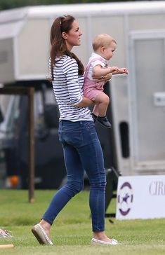 a woman holding a baby in her arms while standing on top of a lush green field