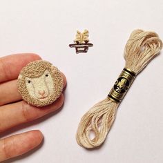 a hand holding a piece of yarn next to a button with a sheep on it