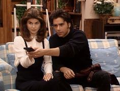 a man and woman sitting on top of a blue couch holding remotes in their hands